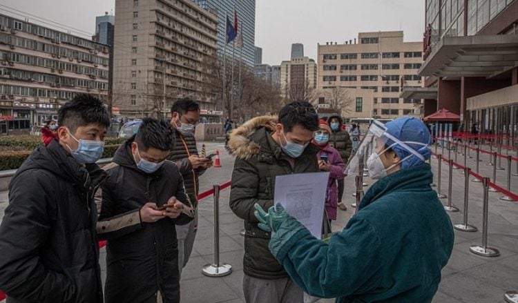 Εργαζόμενη σε νοσοκομείο του Πεκίνου, φορώντας προστατευτικό εξοπλισμό, ελέγχει πολίτες που φθάνουν εκεί για να ελεγχθούν για Covid-19. Εικόνες σαν κι αυτή είναι καθημερινές σε όλη την Κίνα (φωτ.: EPA/ROMAN PILIPEY)