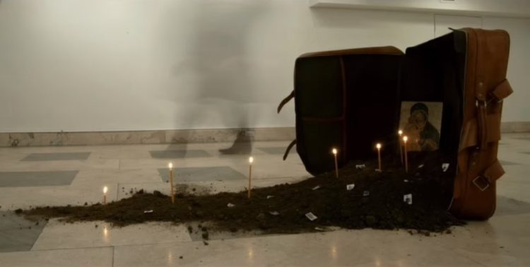 Εγκατάσταση χώμα, βαλίτσα, κεριά, εικόνα, γραμματόσημα, διαστάσεις μεταβλητές. Το 2019 στο Ελληνικό Γενικό Προξενείο της Νέας Υόρκης. Έργο και φωτογραφία του Γιώργου Ταξίδη