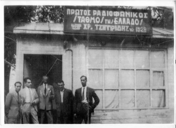 Εξωτερική άποψη του στούντιο που δεν ήταν  παρά μια παράγκα. Στην είσοδο φωτογραφίζεται ο
Χρήστος Τσιγγιρίδης (κέντρο) με μερικούς συνεργάτες του (πηγή: radiomuseum.gr/tsiggiridis)