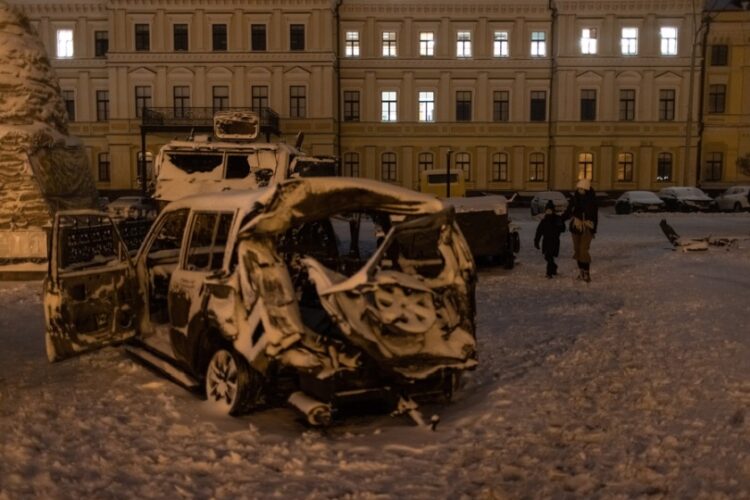 Γυναίκα με το παιδί της προσπερνούν κατεστραμμένα αυτοκίνητα και ρωσικά στρατιωτικά οχημάτα σε πλατεία του Κιέβου (φωτ. EPA/Roman Pilipey)