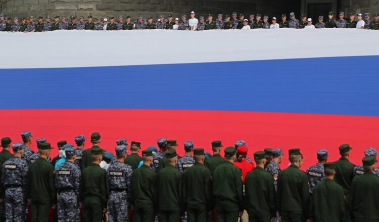 Ρώσοι στρατιώτες κρατούν μια τεράστια σημαία της Ρωσίας, στη διάρκεια εθνικής επετείου. Σύμφωνα με τις εκτιμήσεις του BBC, στη διάρκεια της εισβολής στην Ουκρανία, η Ρωσία θα μπορούσε να έχει περισσότερους από 24.000 νεκρούς (φωτ.: EPA/Maxim Shipenkov)