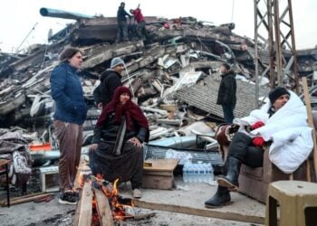 Με φόντο κατεστραμμένα κτήρια άνθρωποι προσπαθούν να ζεσταθούν γύρω από μια φωτιά (φωτ.: EPA/Erdem Sahin)