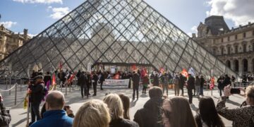 Επισκέπτες και τουρίστες περιμένουν έξω από το Λούβρο, απέναντι από τους διαδηλωτές που απέκλεισαν την είσοδο του μουσείου, προκειμένου να διαμαρτυρηθούν για τη διετή αύξηση των ορίων συνταξιοδότησης, στο πλαίσιο εκτεταμένων κινητοποιήσεων σε ολόκληρη τη Γαλλία (φωτ.: EPA/Christophe Petit Tesson)