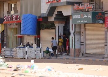 Σουδανοί στέκονται μπροστά από ένα κατάστημα στο Χαρτούμ. Στο δρόμο διακρίνονται συντρίμμια από τις συγκρούσεις που προηγήθηκαν ανάμεσα στις δυνάμεις του στρατού και τους παραστρατιωτικούς (φωτ.: EPA/Stringer)