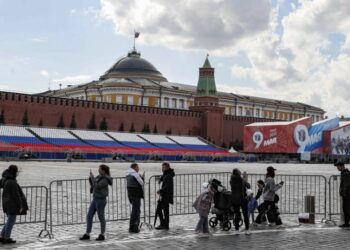 Πολίτες στέκονται μπροστά από τις προετοιμασίες της παρέλασης της 9ης Μαΐου, έξω από το Κρεμλίνο, όπου κυματίζει η σημαία του Ρώσου προέδρου (φωτ.: EPA/Yuri Kochetkov)