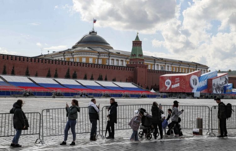 Πολίτες στέκονται μπροστά από τις προετοιμασίες της παρέλασης της 9ης Μαΐου, έξω από το Κρεμλίνο, όπου κυματίζει η σημαία του Ρώσου προέδρου (φωτ.: EPA/Yuri Kochetkov)
