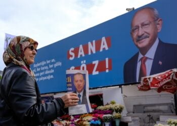 Γυναίκα μοιράζει φυλλάδια του Ρετζέπ Ταγίπ Ερντογάν μπροστά από αφίσα του Κεμάλ Κιλλιτσντάρογλου στην Κωνσταντινούπολη (φωτ.: EPA/Sedat Suna)