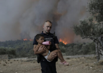 Ο αστυφύλακας Παύλος Τερζόγλου μεταφέρει στην αγκαλιά ένα παιδί κατά τη διάρκεια πυρκαγιάς σε δασική έκταση στο Πουρνάρι Δερβενοχωρίων (φωτ.: ΑΠΕ-ΜΠΕ / Κώστας Τσιρώνης)