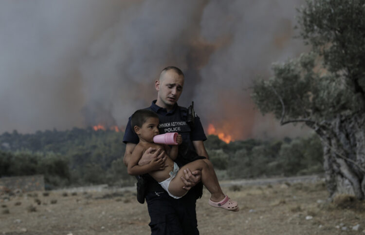 Ο αστυφύλακας Παύλος Τερζόγλου μεταφέρει στην αγκαλιά ένα παιδί κατά τη διάρκεια πυρκαγιάς σε δασική έκταση στο Πουρνάρι Δερβενοχωρίων (φωτ.: ΑΠΕ-ΜΠΕ / Κώστας Τσιρώνης)