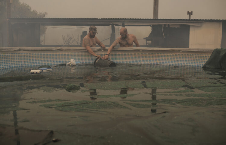 Τα αδέλφια Στάθη, Σταμάτης και Σπύρος, μεταφέρουν νερό από πισίνα στην προσπάθεια τους να περιορίσουν τη φωτιά που απειλεί το αγρόκτημα τους στην περιοχή Παλαιοκούντουρα Δερβενοχωρίων (φωτ.: ΑΠΕ-ΜΠΕ / Κώστας Τσιρώνης)