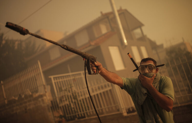 Πολίτης φορώντας μάσκα καταδύσεων και χρησιμοποιώντας πιεστικό ρίχνει νερό σε σπίτι κατά τη διάρκεια της πυρκαγιάς στο Λαγονήσι (φωτ.: ΑΠΕ-ΜΠΕ / Κώστας Τσιρώνης)