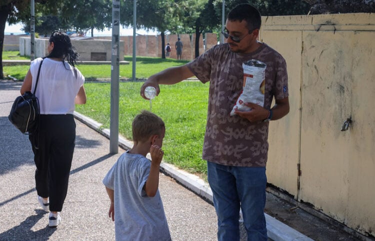 Άνδρας ρίχνει νερό στο κεφάλι του παιδιού για να δροσιστεί (φωτ.: ΑΠΕ-ΜΠΕ / Νίκος Αραμπατζής)
