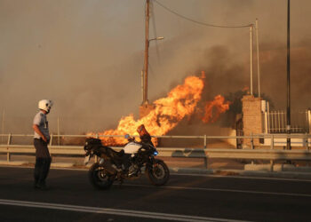 Αστυνομικός κοιτάζει φωτιά που καίει την αυλή σπιτιού στο Λαγονήσι (φωτ.: ΑΠΕ-ΜΠΕ / Ορέστης Παναγιώτου)
