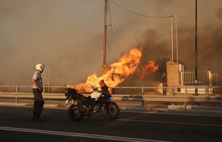 Αστυνομικός κοιτάζει φωτιά που καίει την αυλή σπιτιού στο Λαγονήσι (φωτ.: ΑΠΕ-ΜΠΕ / Ορέστης Παναγιώτου)
