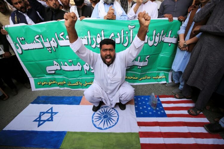 Άνδρας στην Πεσαβάρ του Πακιστάν κάθεται πάνω στις σημαίες της Ινδίας, του Ισραήλ και των ΗΠΑ κατά τη διάρκεια διαδήλωσης υποστήριξης των Παλαιστινίων (φωτ.: EPA/ ARSHAD ARBAB)