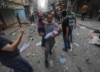Παλαιστίνιος κρατά ένα μωρό κι ένα μικρό κορίτσι ενώ απομακρύνεται από το σημείο όπου χτύπησε ισραηλινή ρουκέτα σε στρατόπεδο προσφύγων μέσα στη Γάζα (φωτ.: EPA-EFE/ Martin Divisek/Mohammed Saber)