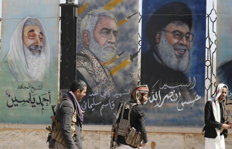 Χούθι περνούν μπροστά από γκράφιτι σε κεντρικό δρόμο της πρωτεύουσας της Υεμένης. Από δεξιά: ο ηγέτης της Χεζμπολάχ Χασάν Νασράλα, ο Ιρανός στρατηγός Κασέμ Σουλεϊμανί που σκοτώθηκε από αμερικανικό πλήγμα, και ο ιδρυτής και πνευματικός ηγέτης της Χαμάς Αχμέντ Γιασίν που σκοτώθηκε το 2004 στη Γάζα (φωτ.: EPA / Yahya Arhab)