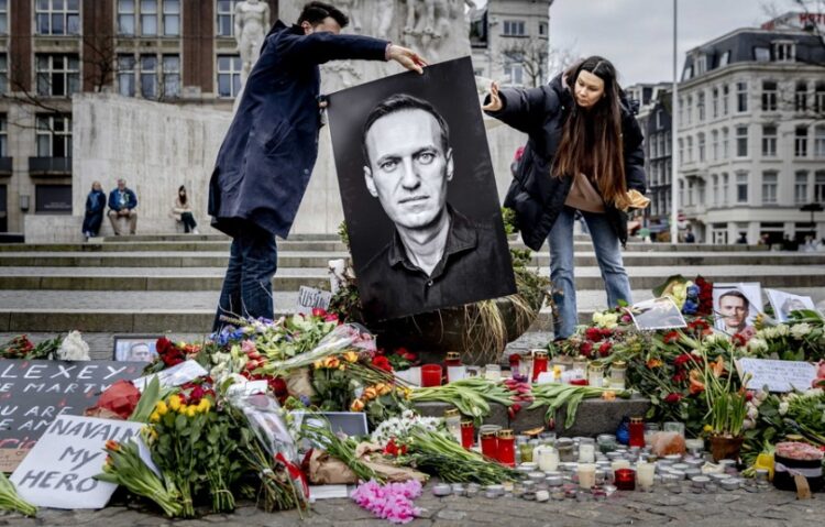 Πολίτες στο Άμστερνταμ κρατούν φωτογραφία του Αλεξέι Ναβάλνι πάνω από λουλούδια που έχουν αφεθεί στη μνήμη του, στη διάρκεια αυτοσχέδιας δέησης για τον ηγέτη της ρωσικής αντιπολίτευσης (φωτ.: EPA/Remko de Waal)
