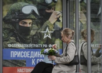 Ρωσίδα κάθεται σε στάση λεωφορείου στη Μόσχα, όπου διαφημιστική αφίσα καλεί τους ενδιαφερόμενους να καταταχθούν στις Ένοπλες Δυνάμεις, «στην αληθινή τους δουλειά» (φωτ.:  EPA/ Yuri Kochetkov)