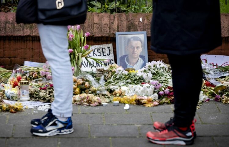 Ρώσοι πολίτες στην Ολλανδία περιμένουν στη σειρά για να ψηφίσουν στην πρεσβεία τους στη Χάγη, ενώ πίσω τους διακρίνεται φωτογραφία του Αλεξέι Ναβάλνι μαζί με λουλούδια που τοποθετήθηκαν στη μνήμη του (φωτ.: EPA/Robin Van Lonkhuijsen)