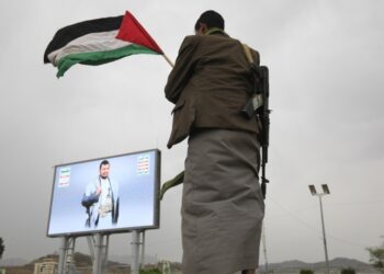 Ένοπλος Χούθι κρατά παλαιστινιακή σημεία μπροστά από μια αφίσα του ηγέτη του κινήματος Αμπνούλ Μαλίκ αλ Χούθι, στη διάρκεια διαμαρτυρίας ενάντια στις ΗΠΑ και το Ισραήλ (φωτ.: EPA/Yahya Arhab)