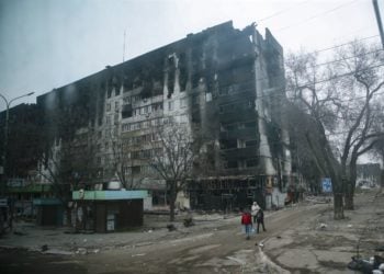 Ουκρανοί μεταφέρουν νερό περνώντας δίπλα από ένα καμμένο και κατεστραμμένο κτήριο, στη Μαριούπολη (φωτ. αρχείου: ΕPA/ Sergei Ilnitsky)