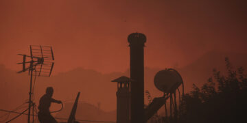 Πολίτης καταβρέχει προληπτικά με νερό την ταράτσα του σπιτιού του (φωτ.: ΑΠΕ-ΜΠΕ / Κώστας Τσιρώνης)