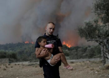 Ο αστυφύλακας Παύλος Τερζόγλου μεταφέρει στην αγκαλιά ένα παιδί κατά τη διάρκεια πυρκαγιάς σε δασική έκταση στο Πουρνάρι Δερβενοχωρίων (φωτ.: ΑΠΕ-ΜΠΕ / Κώστας Τσιρώνης)