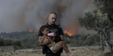 Ο αστυφύλακας Παύλος Τερζόγλου μεταφέρει στην αγκαλιά ένα παιδί κατά τη διάρκεια πυρκαγιάς σε δασική έκταση στο Πουρνάρι Δερβενοχωρίων (φωτ.: ΑΠΕ-ΜΠΕ / Κώστας Τσιρώνης)