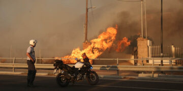 Αστυνομικός κοιτάζει φωτιά που καίει την αυλή σπιτιού στο Λαγονήσι (φωτ.: ΑΠΕ-ΜΠΕ / Ορέστης Παναγιώτου)