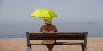 Μία γυναίκα σε παγκάκι κρατά ομπρέλα για να προστατευθεί από τον ήλιο στην παραλία της Θεσσαλονίκης (φωτ.: ΑΠΕ-ΜΠΕ/Αχιλλέας Χήρας)