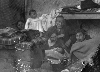 Πρόσφυγες από τη Μικρά Ασία σε πρόχειρο κατάλυμα. Στο κέντρο διακρίνεται μια μητέρα αγκαλιά με το νεογέννητο μωρό της. Αθήνα, 1922 (φωτ.: Π. Πουλίδης / Αρχείο ΕΡΤ)