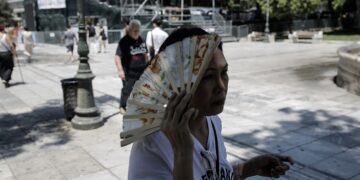 Γυναίκα χρησιμοποιεί τη βεντάλια της για να καλυφθεί από τον ήλιο καθώς διασχίζει την πλατεία Συντάγματος (φωτ.: ΑΠΕ-ΜΠΕ / Κώστας Τσιρώνης)