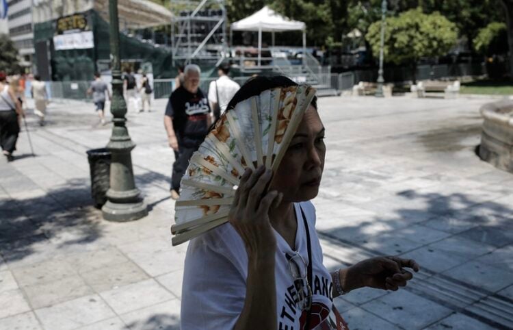 Γυναίκα χρησιμοποιεί τη βεντάλια της για να καλυφθεί από τον ήλιο καθώς διασχίζει την πλατεία Συντάγματος (φωτ.: ΑΠΕ-ΜΠΕ / Κώστας Τσιρώνης)
