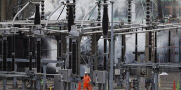 Εργαζόμενοι προσπαθούν να αποκαταστήσουν τις ζημιές που προκάλεσε η πυρκαγιά σε κοντινό υποσταθμό του δικτύου ηλεκτροδότησης στο αεροδρόμιο Χίθροου (φωτ.: EPA/Tolga Akmen)