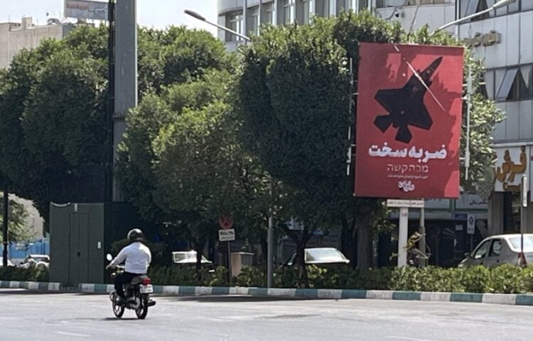 Ιρανός στην Τεχεράνη προσπερνά αφίσα η οποία αναγράφει «Σκληρή απάντηση» απεικονίζοντας ένα βομβαρδιστικό (φωτ.: EPA/Abedin Taherkenareh)