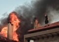 Νεαρός εθελοντής έχει σκαρφαλώσει σε στέγη σπιτιού για να βοηθήσει στην κατάσβεση της φωτιάς (φωτ.: EUROKINISSI/Κώστας Τζούμας)