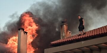 Νεαρός εθελοντής έχει σκαρφαλώσει σε στέγη σπιτιού για να βοηθήσει στην κατάσβεση της φωτιάς (φωτ.: EUROKINISSI/Κώστας Τζούμας)