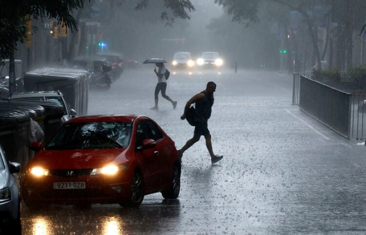 Άνθρωποι προσπαθούν να προστατευθούν από τη βροχή, στη Βαρκελόνη (φωτ.: EPA / Alberto Estevez)