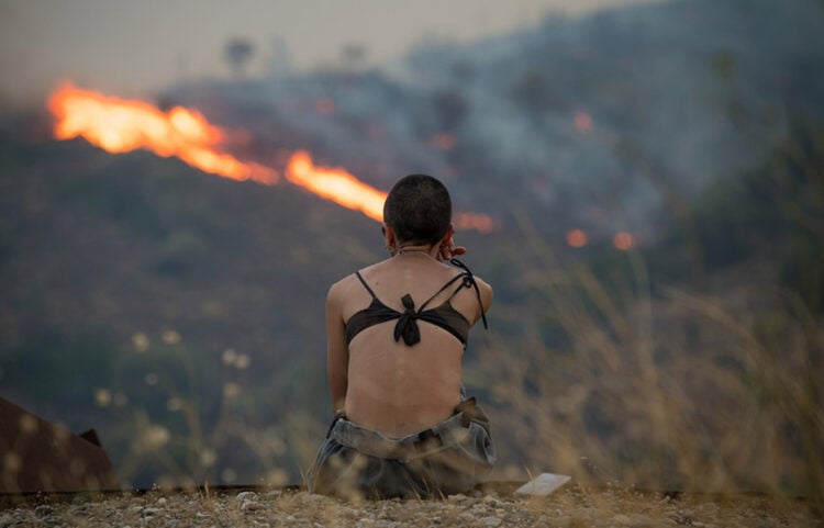 Γυναίκα κοιτάζει τις φλόγες από την πυρκαγιά στην περιοχή Ποταμιά-Πισπιλούντα στη βόρεια Χίο. Τρίτη 12 Αυγούστου 2025 (φωτ.: ΑΠΕ-ΜΠΕ / Κώστας Κουργιάς)