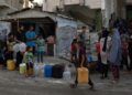 Εκτοπισμένοι Παλαιστίνιοι περιμένουν στην ουρά για να γεμίσουν δοχεία με πόσιμο νερό μετά την καταστροφή του καταυλισμού Χαν Γιουνίς στη νότια Γάζα (φωτ.: EPA/Haitham Imad)