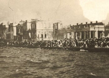 Στην αποβάθρα της Σμύρνης περιμένοντας τη σωτηρία. Πίσω διακρίνεται η καμένη πόλη (πηγή: Φωτογραφικό Αρχείο ΙΕΕΕ / Εθνικό Ιστορικό Μουσείο)