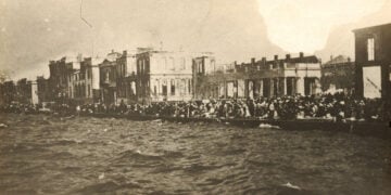 Στην αποβάθρα της Σμύρνης περιμένοντας τη σωτηρία. Πίσω διακρίνεται η καμένη πόλη (πηγή: Φωτογραφικό Αρχείο ΙΕΕΕ / Εθνικό Ιστορικό Μουσείο)