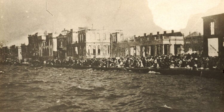 Στην αποβάθρα της Σμύρνης περιμένοντας τη σωτηρία. Πίσω διακρίνεται η καμένη πόλη (πηγή: Φωτογραφικό Αρχείο ΙΕΕΕ / Εθνικό Ιστορικό Μουσείο)