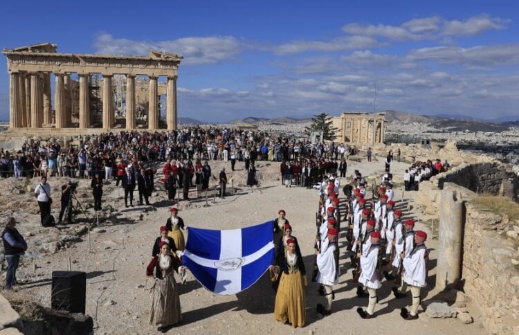 Μέλη της χορευτικής ομάδας του Λυκείου Ελληνίδων με εθνικές ενδυμασίες, κρατώντας τη Σημαία της Απελευθέρωσης και πλαισιωμένα από μαθητές και μαθήτριες της Ιονίου Σχολής, προσήλθαν στο σημείο του ιστού (φωτ.: EUROKINISSI/Γιώργος Κονταρίνης)