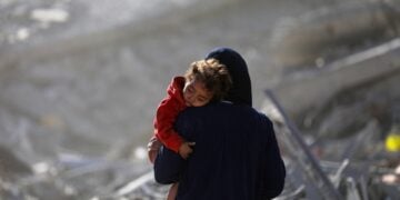 Παλαιστίνια μητέρα κρατά το παιδί της αγκαλιά ενώ περνά μέσα από ερείπια κτηρίων στην πόλη της Γάζας (φωτ.: EPA/Mohammed Saber)