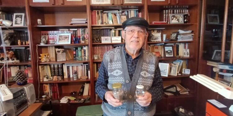 Ο Πέτρος Σιδηρόπουλος στο γραφείο του, κρατώντας γη και ύδωρ από την Πατρίδα, το Κιουλαπέρτ του Καρς (φωτ.: Αλεξία Ιωαννίδου)