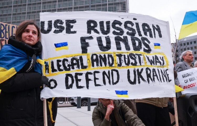 Ουκρανοί κρατούν πανό που αναγράφει «Χρησιμοποιείστε ρωσικά κεφάλαια: Ένας νόμιμος και σωστός τρόποος να υπερασπιστείτε την Ουκρανία» έξω από το κτήριο όπου συνεδριάζει το Ευρωπαϊκό Συμβούλιο των υπουργών Οικονομικών στις Βρυξέλλες (φωτ.: EPA/Olivier Hoslet)