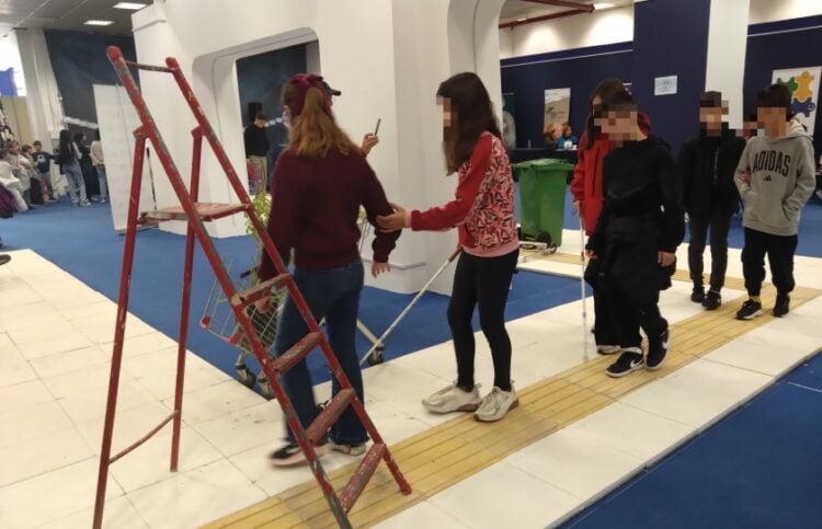 Παιδιά που μετέχουν στη δράση είτε κρατούν το λευκό μπαστούνι, είτε συνοδεύουν συμμαθητές τους ανάμεσα σε τεχνητά εμπόδια, προκειμένου να βιώσουν την καθημερινότητα των ατόμων με προβλήματα όρασης (φωτ.: Έλλη Τσολάκη)