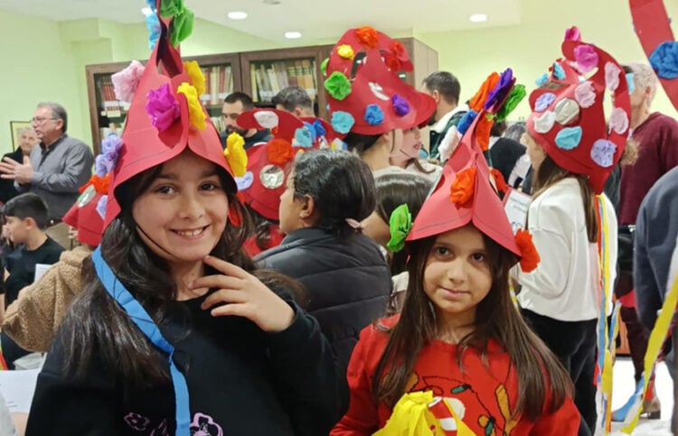 Παρόλο που στο θίασο των Μωμόγερων δεν συμμετέχουν γυναίκες, αυτές εδώ οι μικρές φόρεσαν τις χαρακτηριστικές περικεφαλαίες, έστω και από χαρτί. Στιγμιότυπό από τη δράση στη βιβλιοθήκη της Πτολεμαΐδας (φωτ.: Facebook / Κλαίρη Πλαγερινού)